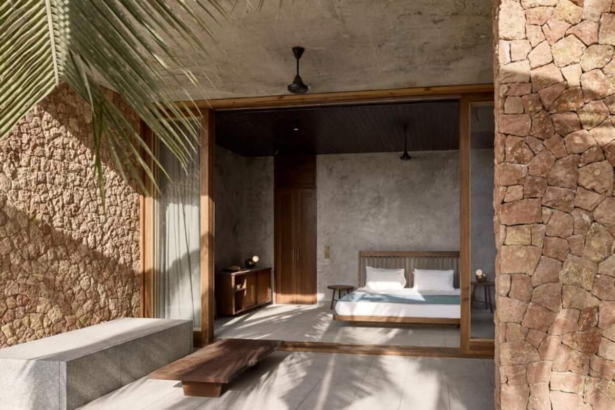 A bedroom with a stone wall, a bed, a wooden bench, and a ceiling fan.