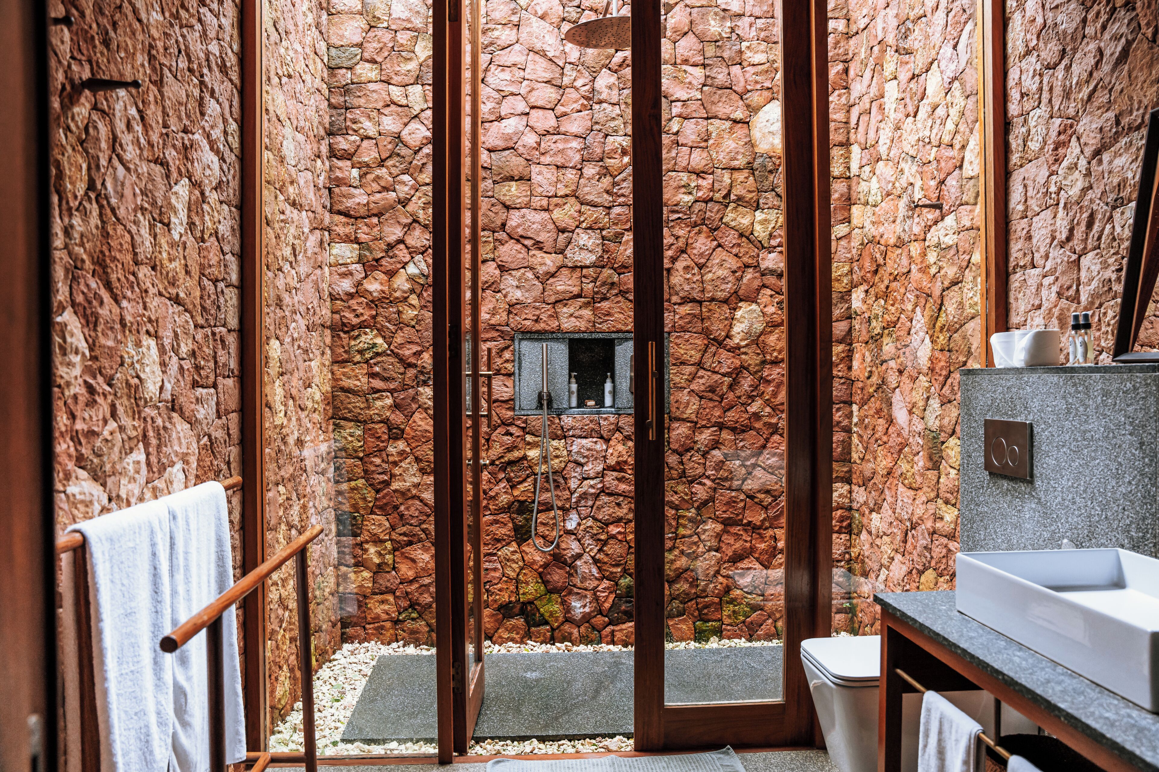 Un baño con pared de piedra, ducha y lavamanos.