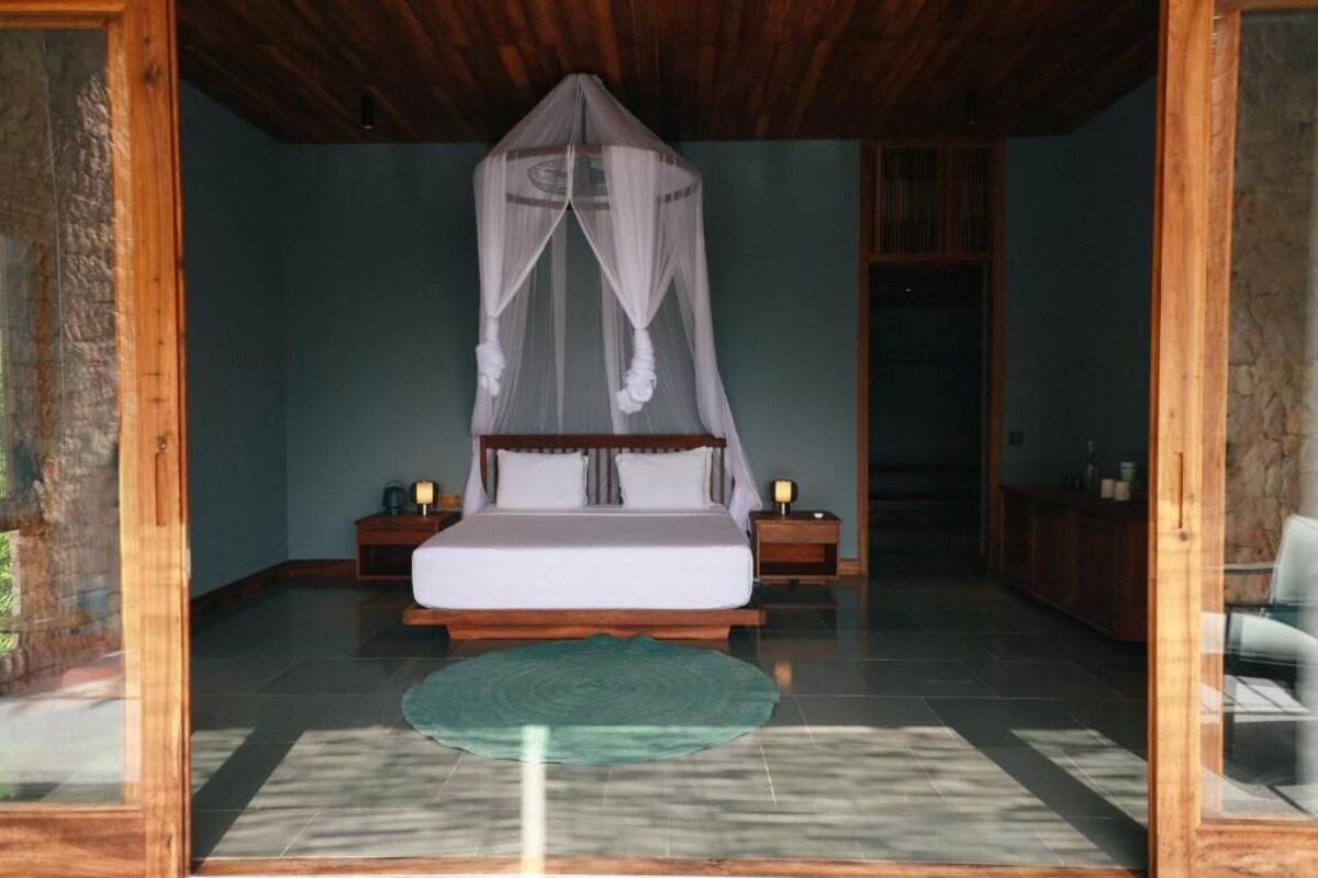 A bedroom with a bed under a canopy, wooden headboard, nightstands, and a green rug.