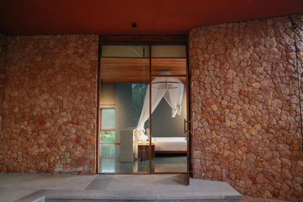 A room with stone walls, a bed with a canopy, and a glass door leading to a balcony.