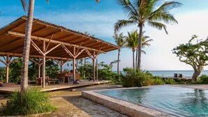 A covered outdoor area with a pool, palm trees, and a view of the ocean.