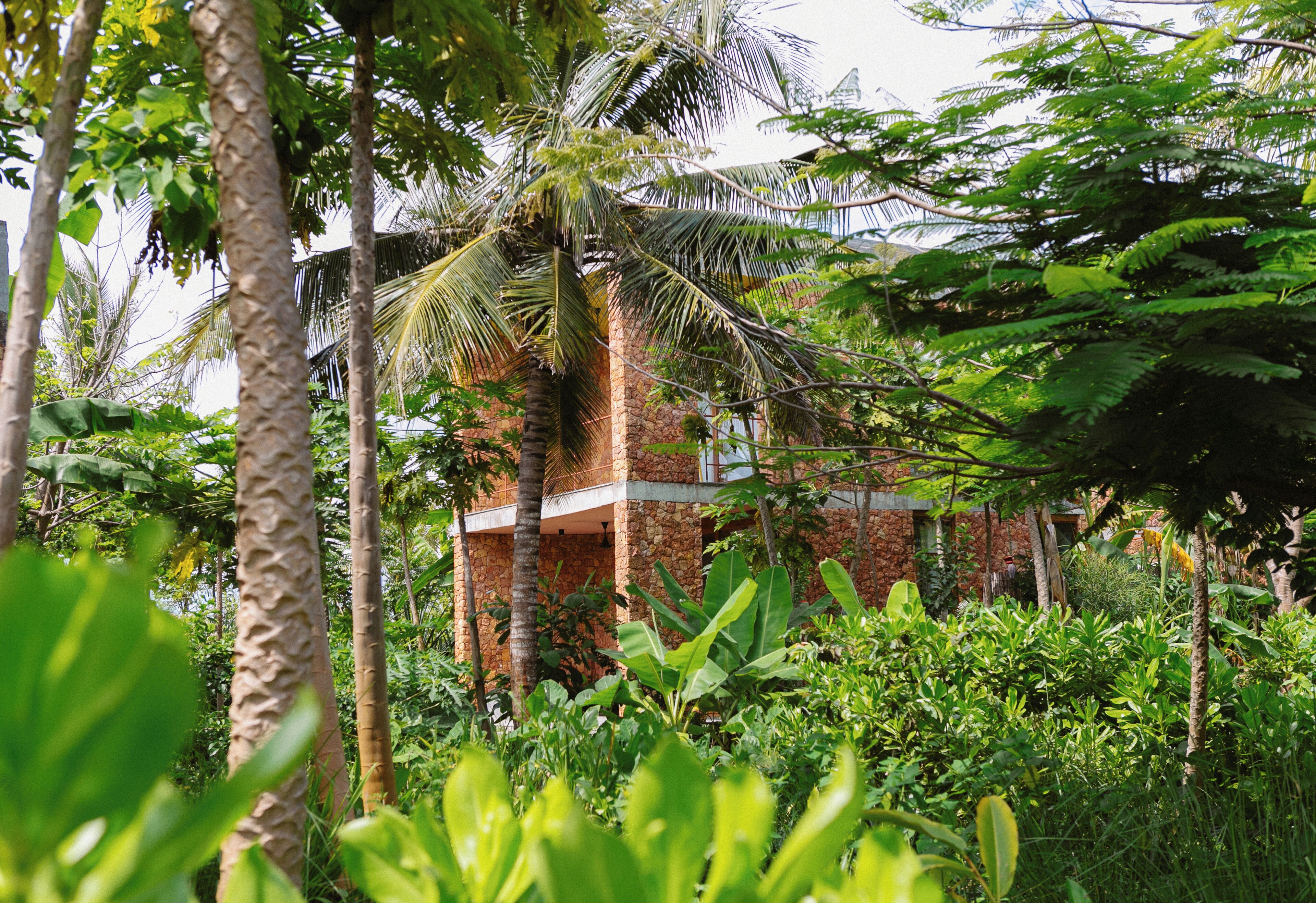 A stone building with a balcony, surrounded by lush greenery and palm trees.
