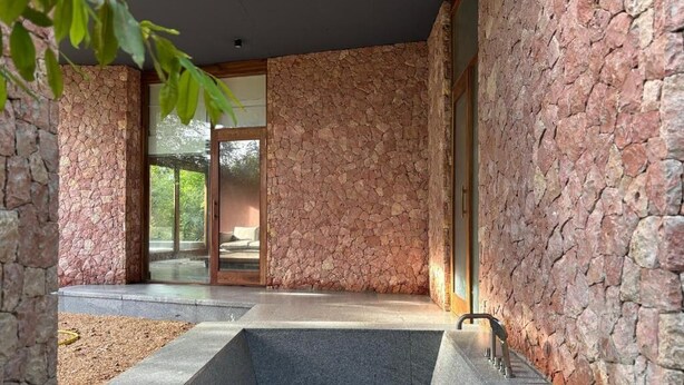 Uma área de spa com parede de pedra, piscina retangular e porta de vidro que dá para área externa.