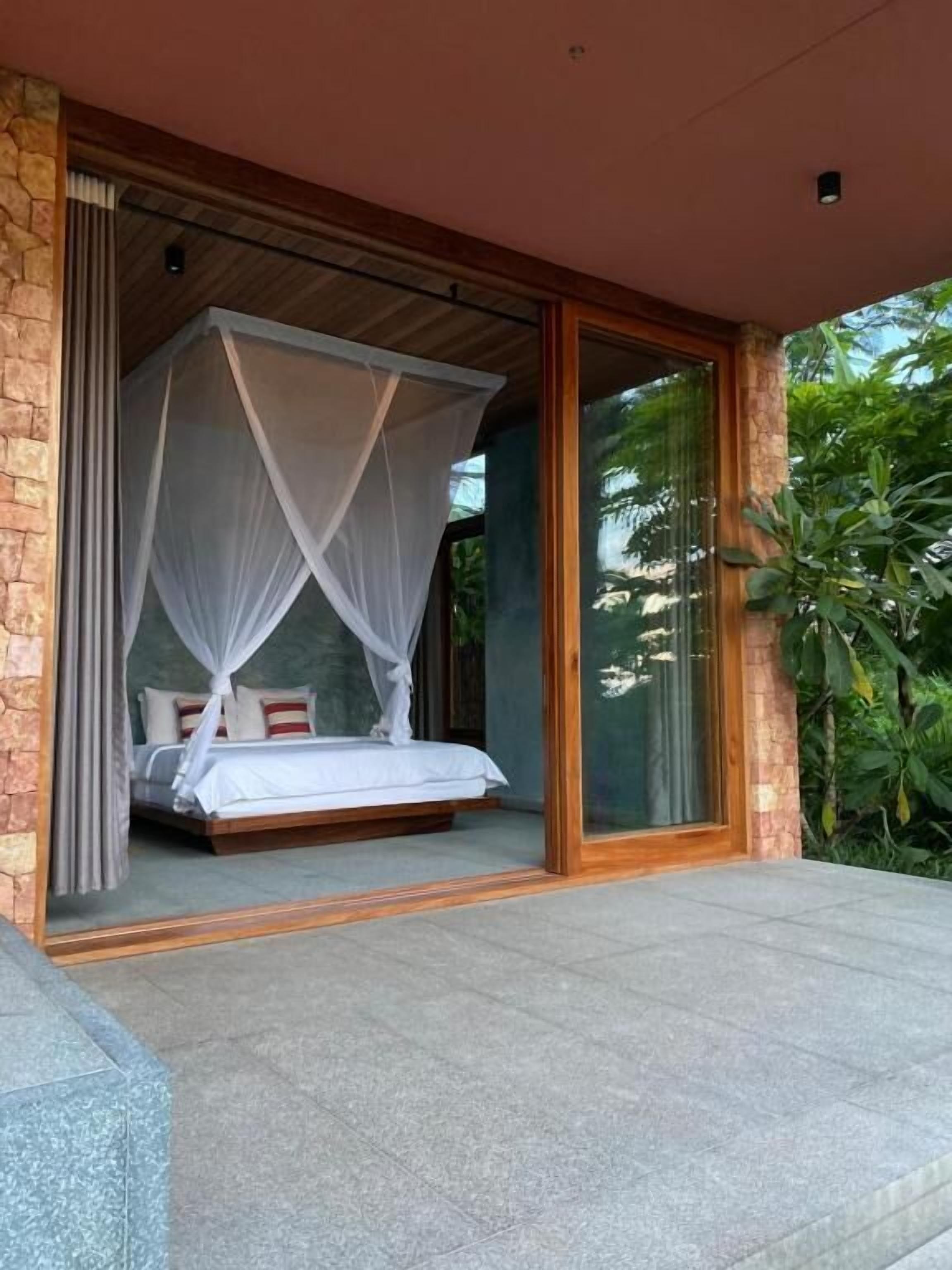 A bedroom with a canopy bed, a stone wall, and a glass door leading to a balcony.