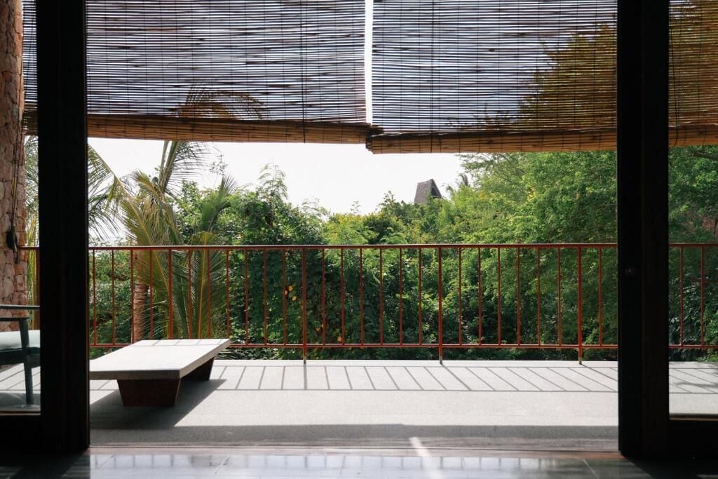 Ein Balkon mit Metallgeländer, einer Sitzbank und Blick auf Grünflächen und Bäume.
