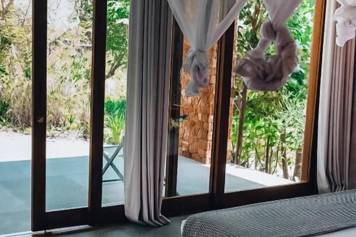 A bedroom with a bed, a canopy, a view of greenery outside, and a stone wall.