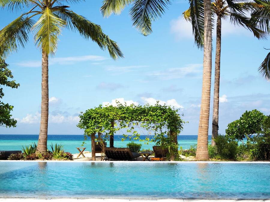Ein Poolbereich mit Liegestühlen und einer Pergola, umgeben von Palmen und Blick auf den Ozean.