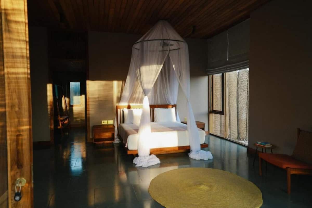 A bedroom with a canopy bed, a round woven rug, and a wooden bench.