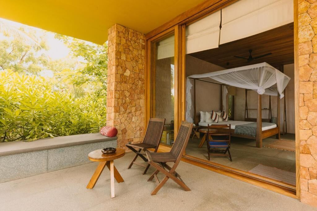 Une chambre avec un lit, une moustiquaire et un balcon équipé de chaises et d’une table.
