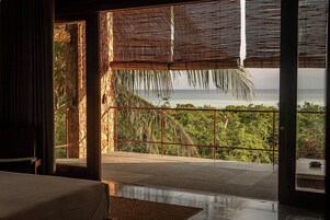 Una habitación con vistas al océano, un balcón con barandilla y una puerta que da al exterior.