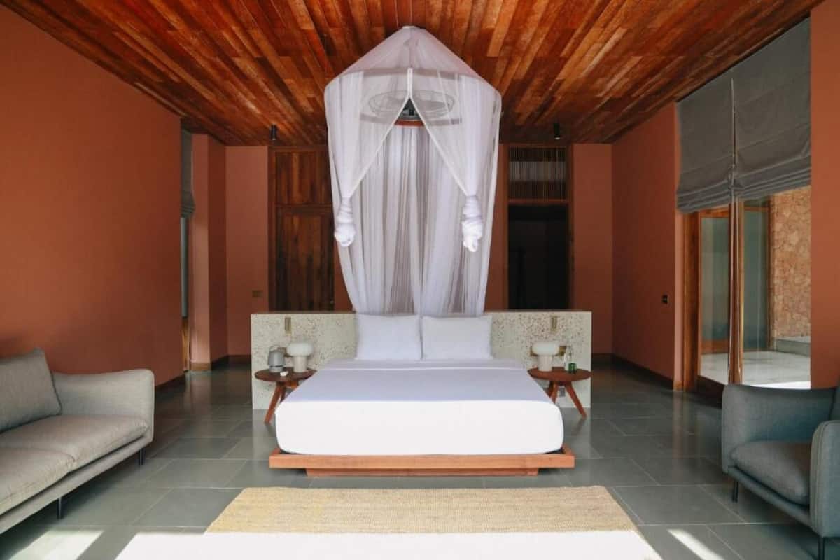 A bedroom with a canopy bed, two nightstands, a sofa, and a large window.