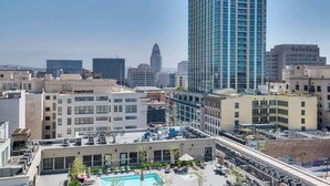 A rooftop pool area with lounge chairs and umbrellas, surrounded by modern buildings and a prominent skyscraper.