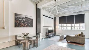 A spacious living room with a large window, a modern sofa, a TV, and a unique metal table.