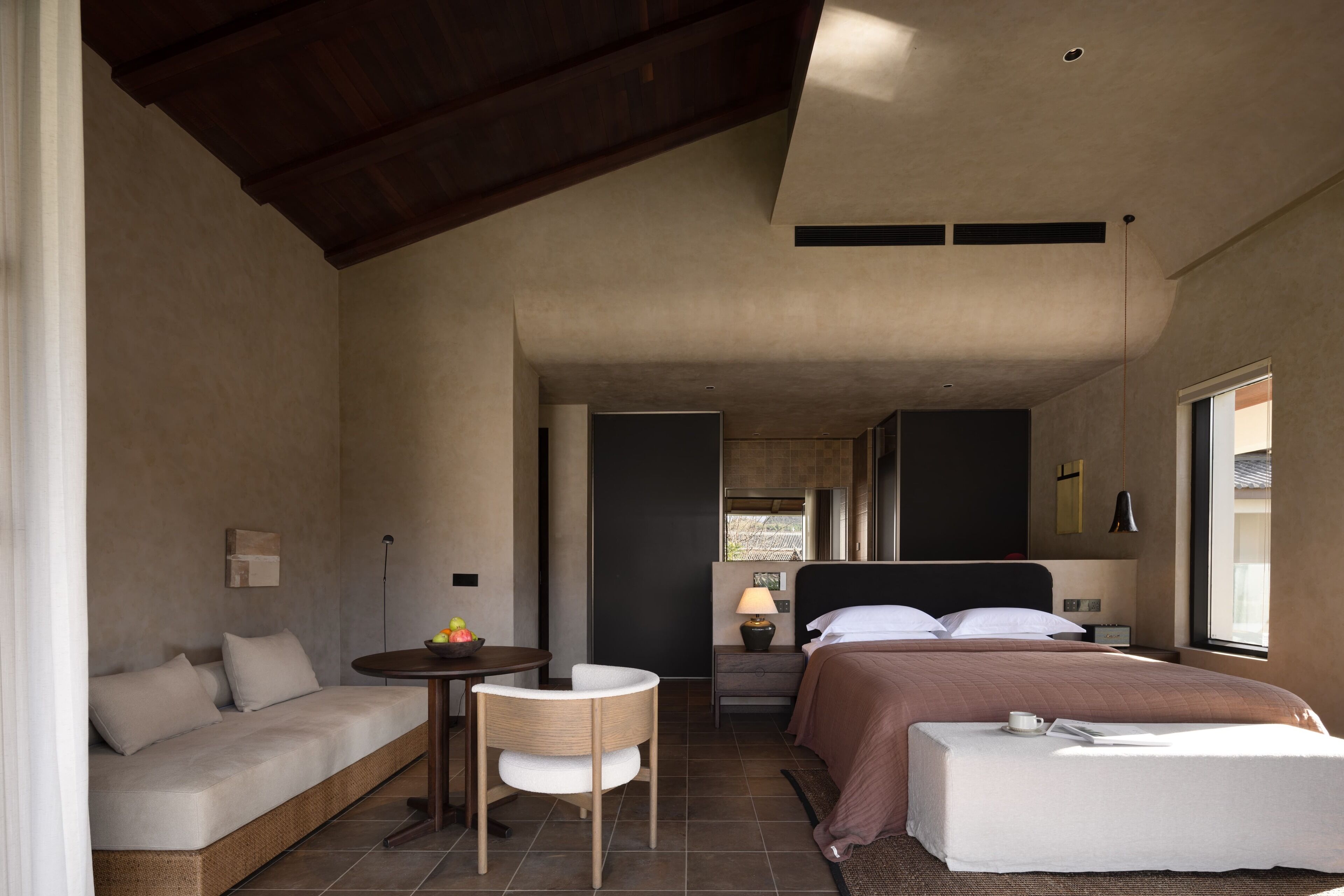 A modern hotel room with a sofa, a small table, a bed, and a window.