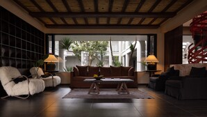 Una sala de estar moderna con un sofá marrón, sillones blancos y una mesa de centro. Hay dos lámparas sobre mesas auxiliares, y un ventanal con vistas a zonas verdes.