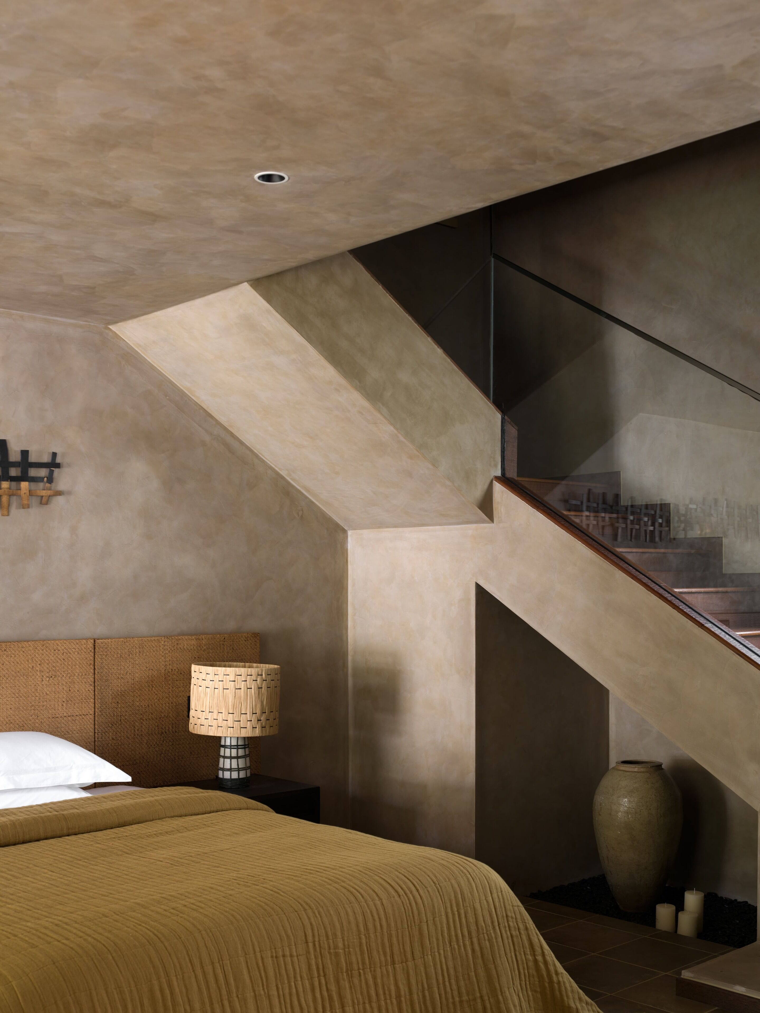 A modern bedroom with a large bed, a nightstand, a lamp, and a vase.