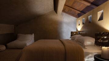 Un dormitorio con techo inclinado, una cama con almohada a rayas, una lámpara de noche y una lámpara de pared.