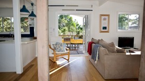 A modern living room with a sofa, TV, and dining area with yellow tablecloths. - Alora Cottage in the heart of Bendalong (Bendalong)