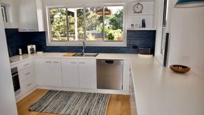 Une cuisine moderne avec des meubles blancs, un lave-vaisselle encastré, une grande fenêtre et un pare-feu bleu.