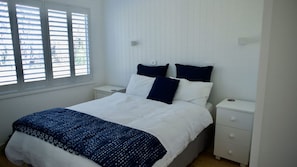 A bedroom with a bed, two bedside tables, and a window with blinds. - Alora Cottage in the heart of Bendalong (Bendalong)