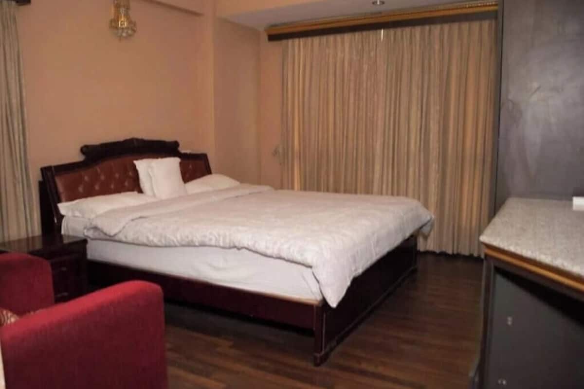 A hotel room with a large bed, a wooden headboard, a red chair, and a desk with a lamp.