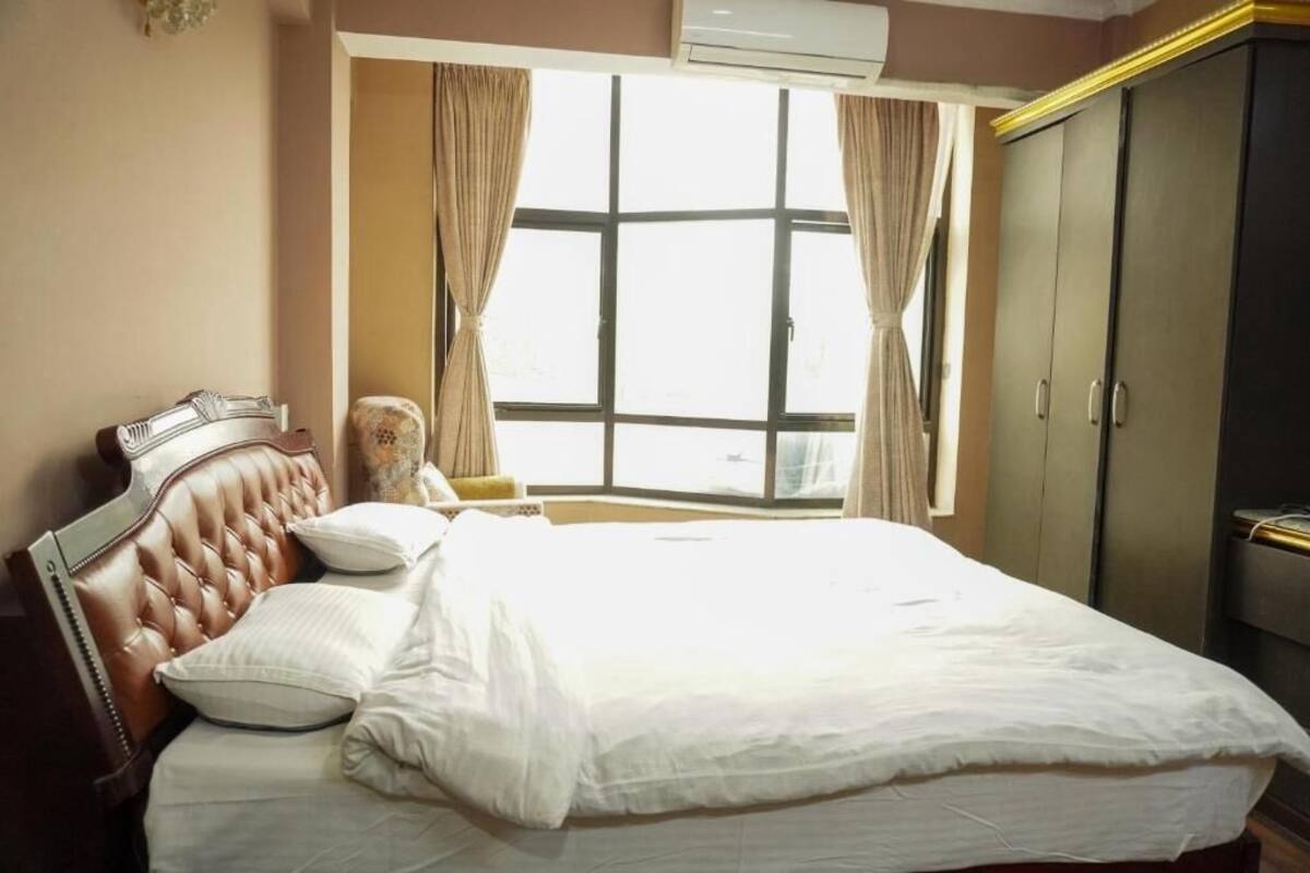 A neatly made bed with white linens, a tufted headboard, and a window with curtains.