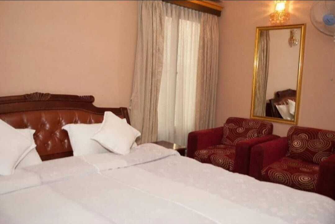 A hotel room with a large bed, a wooden headboard, a red patterned sofa, a mirror, and a window with curtains.