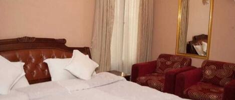 A hotel room with a large bed, a wooden headboard, a red patterned sofa, a mirror, and a window with curtains.