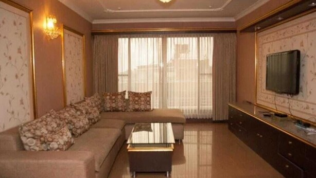 Una sala de estar con un sofá seccional, una mesa de centro, un televisor de pantalla plana y un ventanal con cortinas.