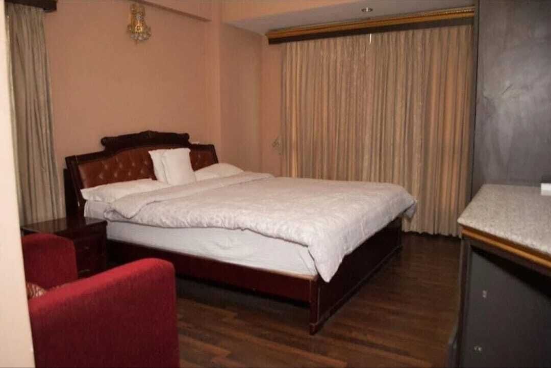 Habitación de hotel con una cama individual, una silla roja, un escritorio y un ventanal con cortinas.