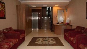 Un vestíbulo de hotel con una zona alfombrada central, dos sofás a cada lado, un mostrador de recepción y una escalera que conduce a otro piso.
