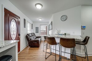 A modern kitchen with a marble countertop, a built-in bar area with stools, a leather sofa, and a large window with blinds. - 1 Mi to Wilmington Riverwalk: Getaway w/ Gas Grill (Wilmington)