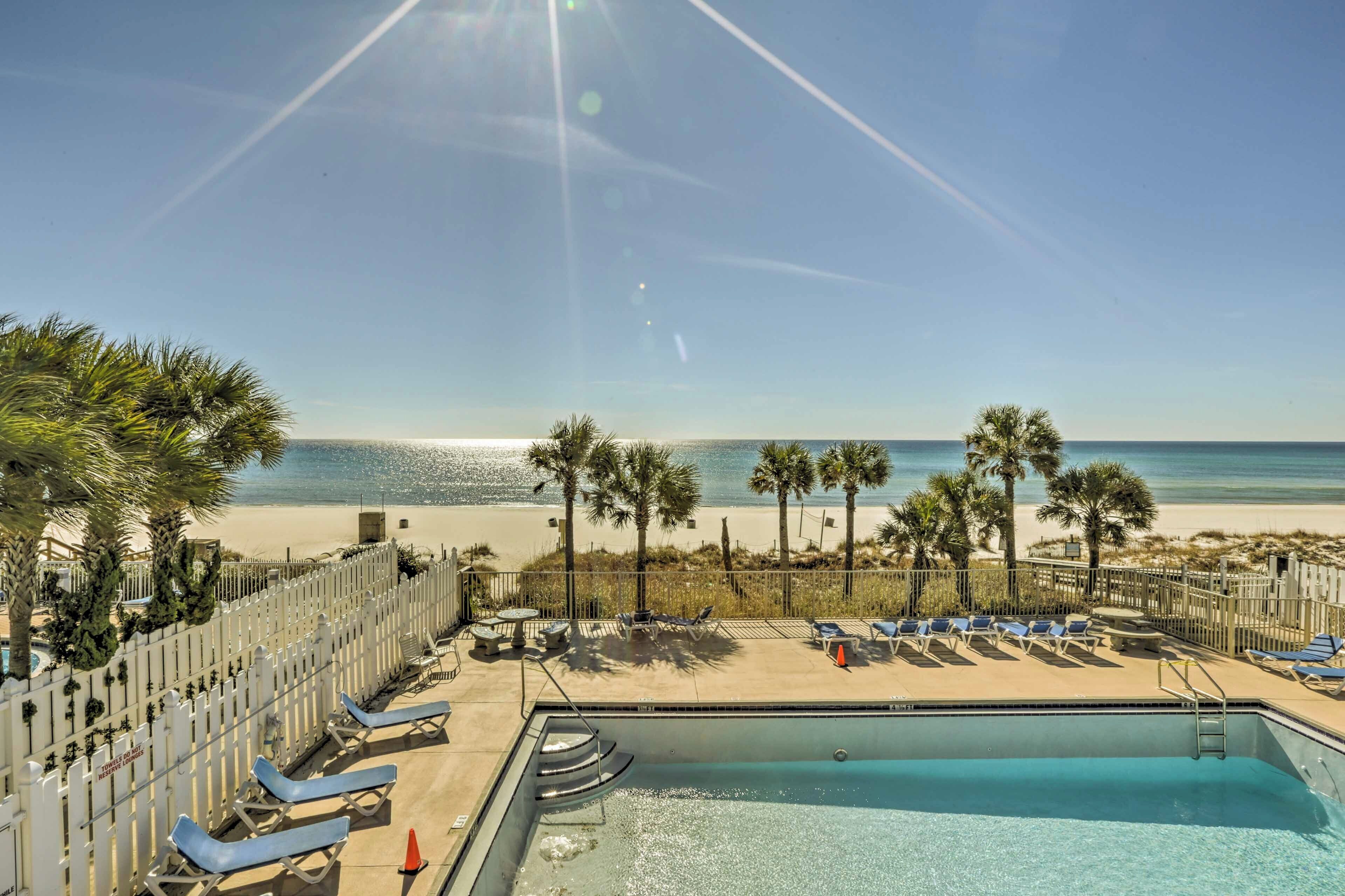 A pool area with lounge chairs, a pool, and a view of the beach and ocean.