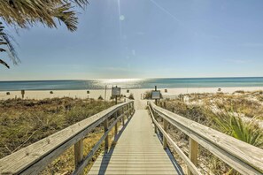 Ein hölzerner Steg führt zu einem Strand mit blauem Himmel und ruhiger See.