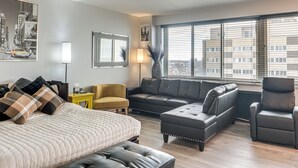 A modern living room with a large bed, two sofas, a chair, and a window with a city view. - 6 Mi to Downtown Cleveland: Lakeview Condo! (Lakewood)