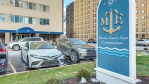 A parking lot with several cars, a sign for Marine Towers East Condominium, and a building with multiple windows in the background. - 6 Mi to Downtown Cleveland: Lakeview Condo! (Lakewood)