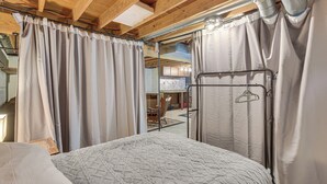 Een slaapkamer met een bed, gordijnen en uitzicht op een eetruimte.