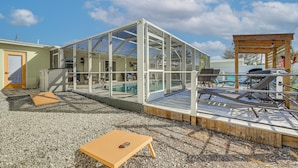 Een glazen constructie met een zwembad, houten terras en een zitgedeelte buiten.