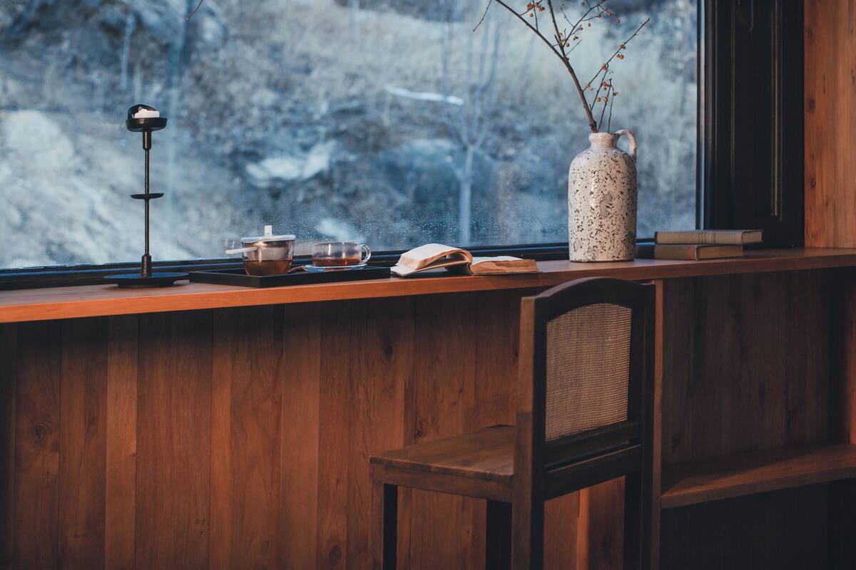 A wooden desk with a book, a teapot, and a vase with branches.