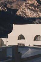 Um edifício moderno com telhado plano e janelas em arco, com montanhas ao fundo.