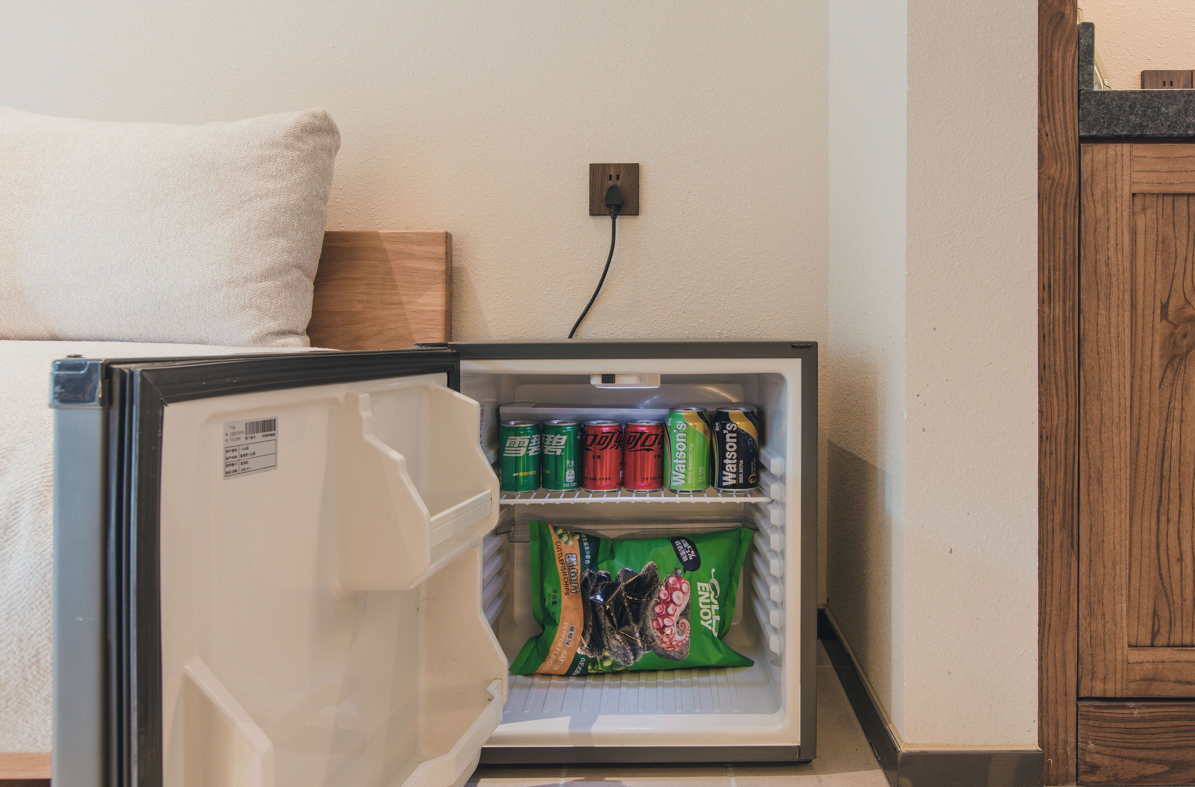 A compact refrigerator with a power outlet above it, containing beverages and snacks.