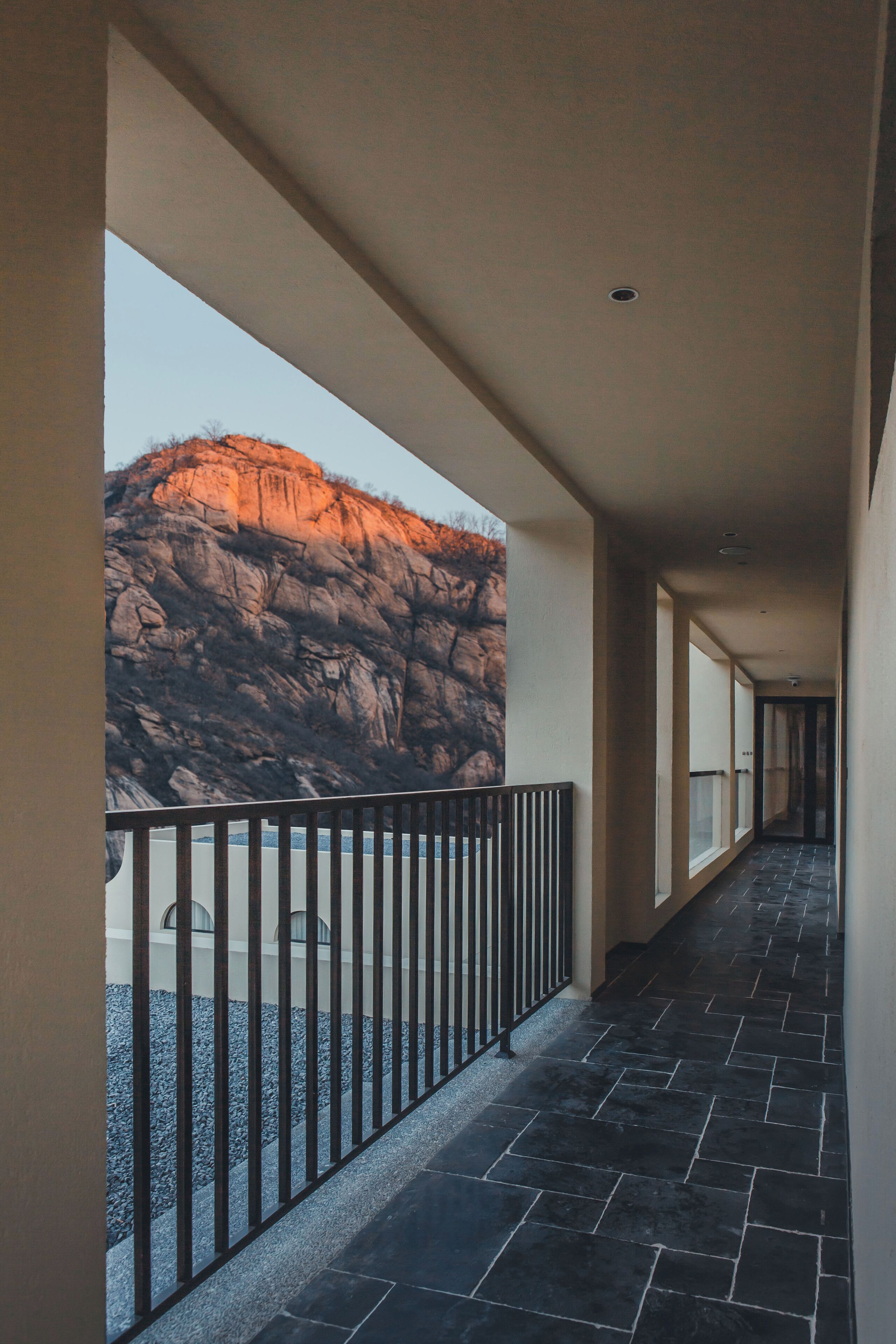 A corridor with a railing, a view of a rocky landscape, and a tiled floor.