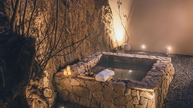 A stone hot tub set against a rocky backdrop with bare trees, surrounded by a gravel area. - Ubaia Hotel (Miyun)
