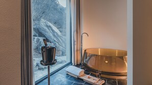 A bathroom with a large bathtub, a window with a view of a snowy landscape, a towel, and a bottle of champagne. - Ubaia Hotel (Miyun)