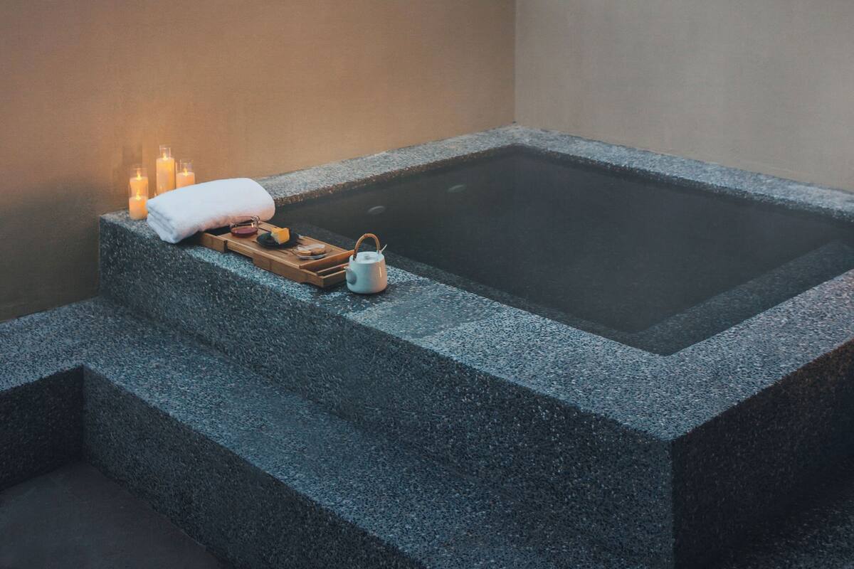 A spa area with a hot tub, candles, and a towel on a stone platform, overlooking a mountainous landscape.