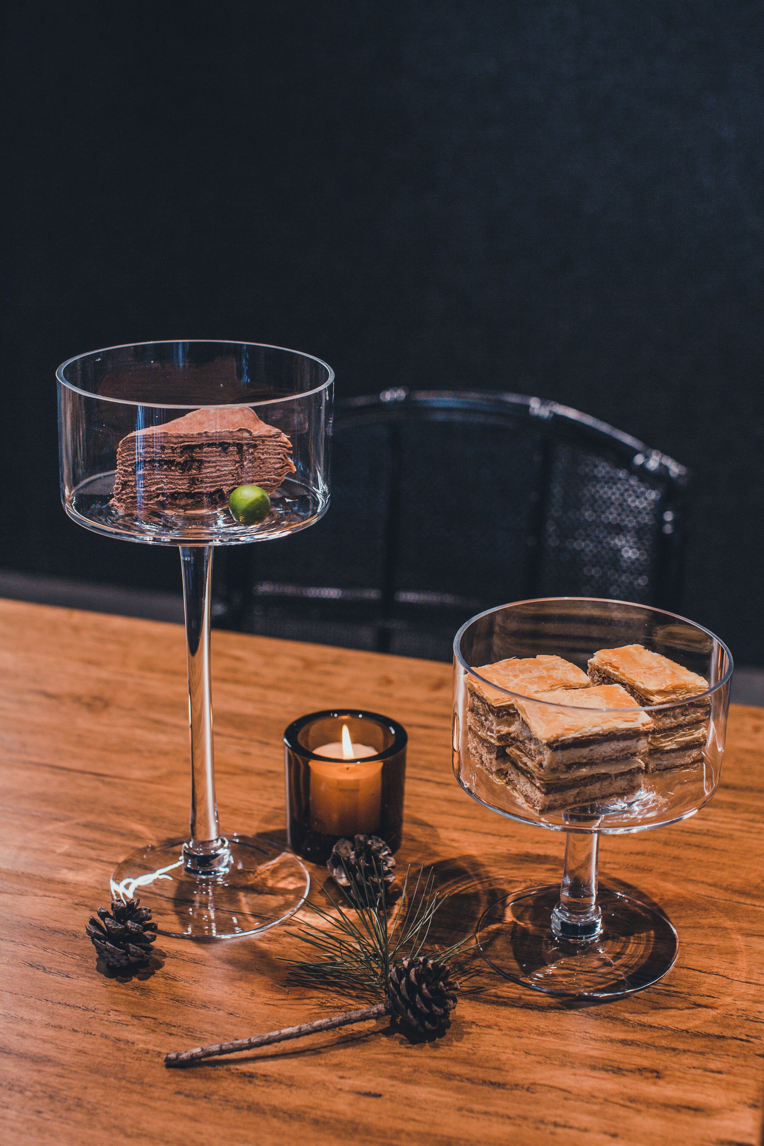 Two dessert glasses on a wooden table with a candle and pine decorations.