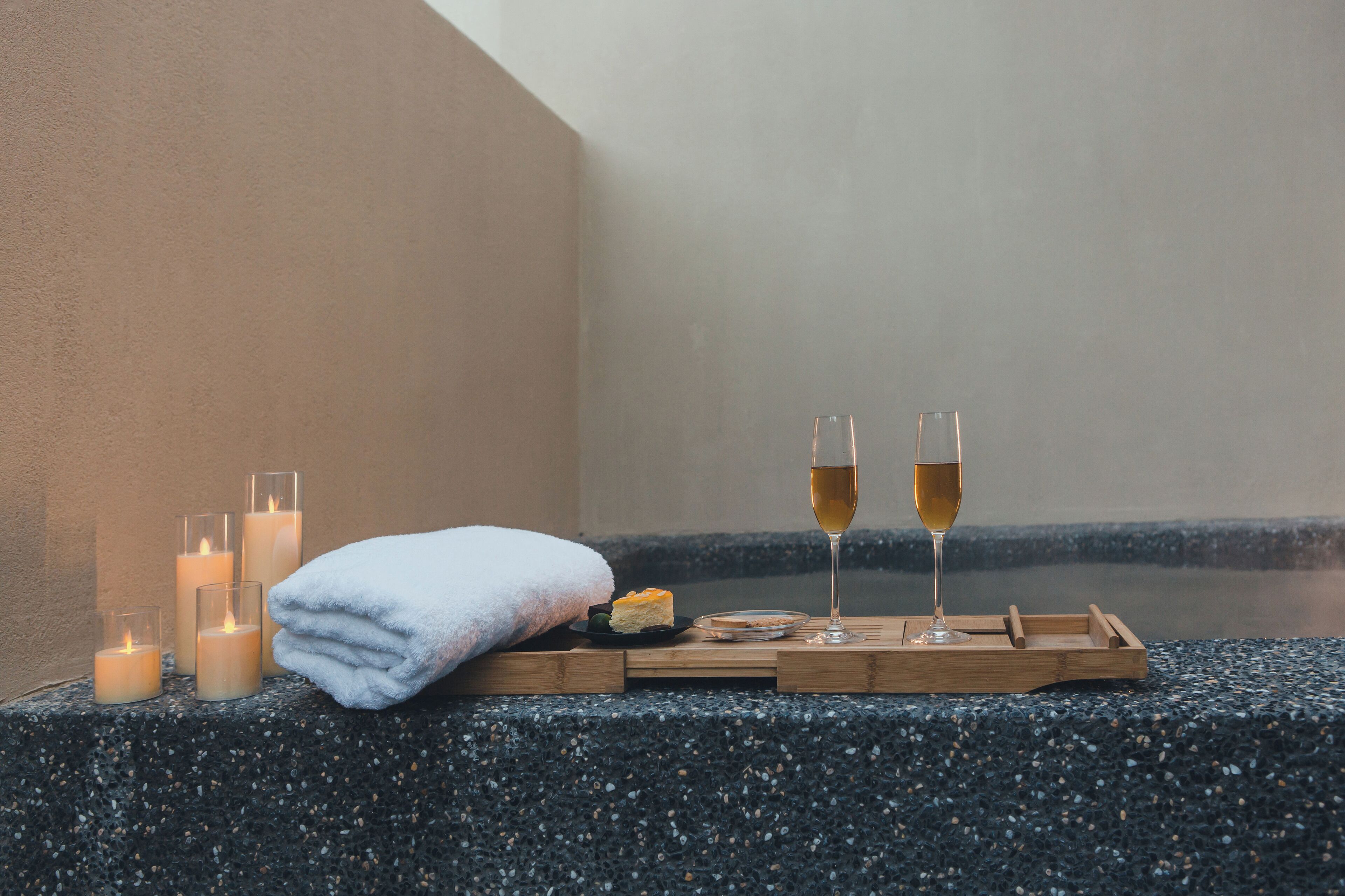 A spa setting with candles, a towel, and glasses of a clear liquid, likely alcohol, on a wooden tray.