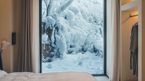 A bedroom with a large bed, a window with a snowy view, and a door to a bathroom. - Ubaia Hotel (Miyun)