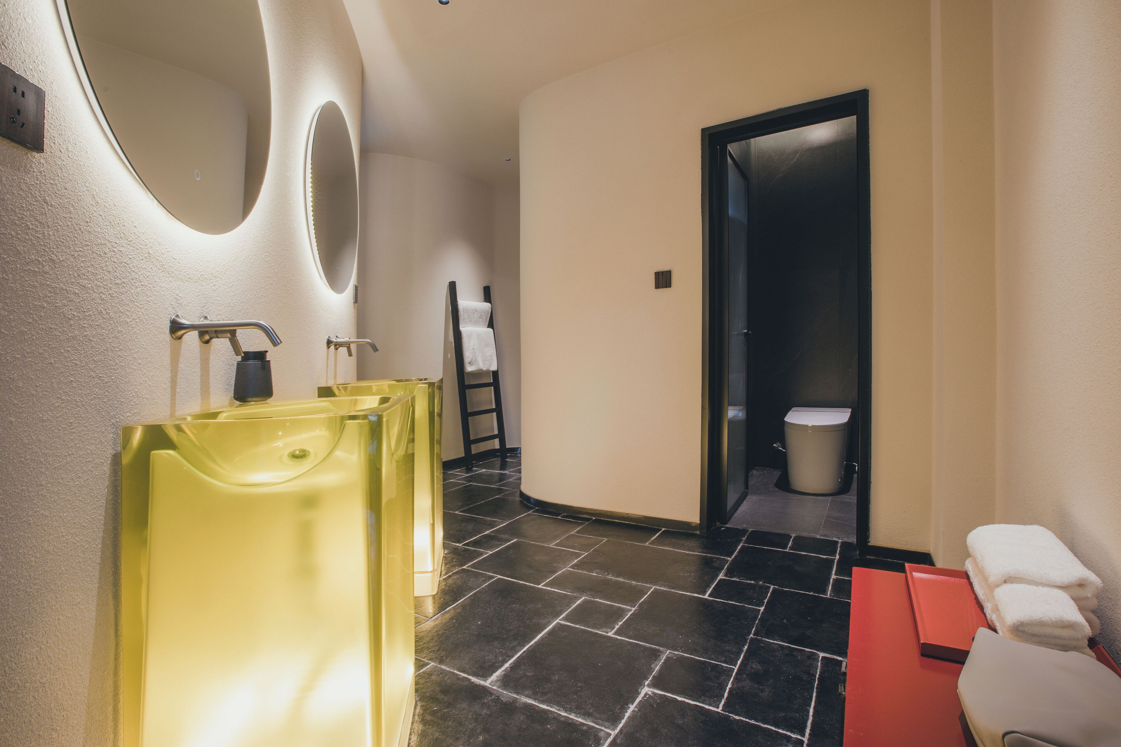 Un baño moderno con un lavamanos amarillo, un espejo y un banco rojo.