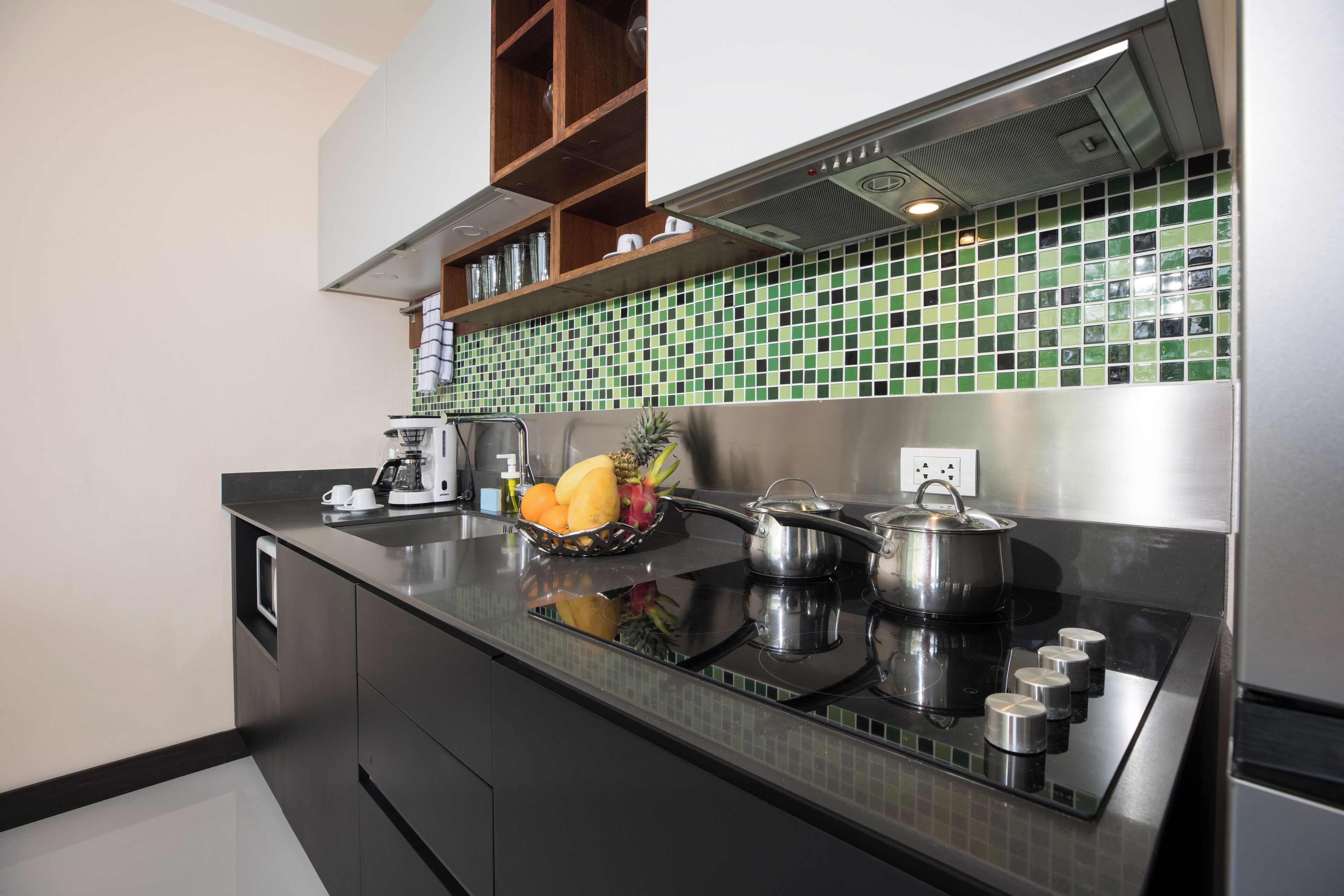 A modern kitchen with a black countertop, stainless steel appliances, and a green-tiled backsplash.